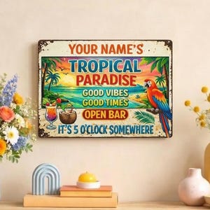 May include: A rectangular metal sign with a tropical theme. The sign features the text "YOUR NAME'S TROPICAL PARADISE" and other phrases like "GOOD VIBES" and "OPEN BAR." A colorful parrot is perched on a branch. The sign has a distressed, vintage look.