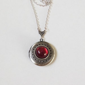 May include: A silver locket necklace with a red glass cabochon. The locket has an ornate design around the edge.