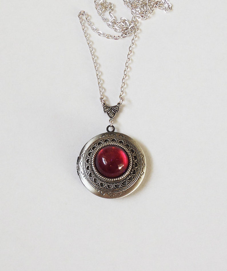 May include: A silver locket necklace with a red glass cabochon. The locket has an ornate design around the edge.