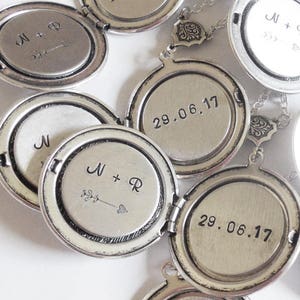 May include: A set of silver locket necklaces with engraved dates and initials. The lockets are open and show the inside of the locket with the engravings. The lockets are connected by a silver chain.