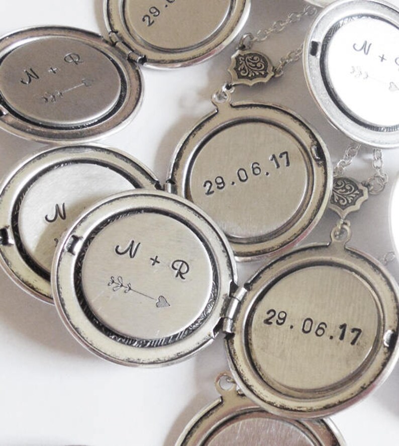 May include: A set of silver locket necklaces with engraved dates and initials. The lockets are open and show the inside of the locket with the engravings. The lockets are connected by a silver chain.