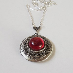 May include: A silver locket necklace with a red glass cabochon. The locket has an ornate design with a filigree border.