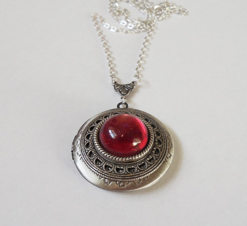 May include: A silver locket necklace with a red glass cabochon. The locket has an ornate design with a filigree border.