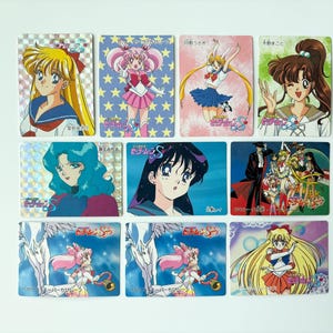 以下が含まれることがあります： アニメのキャラクターが描かれた、カラフルなトレーディングカード9枚。カードには、鮮やかな髪と衣装の様々なキャラクターが、星やその他のデザインの背景に描かれています。カードはグリッド状に配置されています。