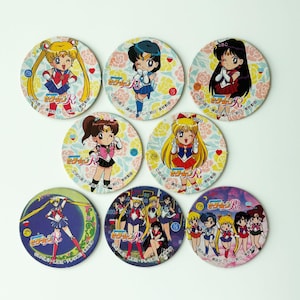 May include: A collection of eight round Sailor Moon character coasters. Each coaster features a different character illustration with Japanese text and floral background. The coasters are colorful and vibrant, perfect for fans.