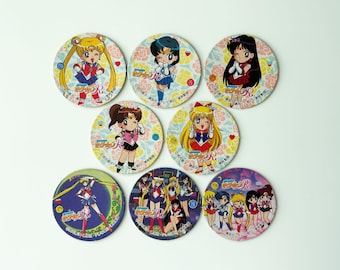 May include: A collection of eight round Sailor Moon character coasters. Each coaster features a different character illustration with Japanese text and floral background. The coasters are colorful and vibrant, perfect for fans.