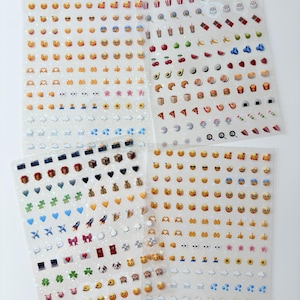 May include: Three transparent sticker sheets featuring a wide variety of small, colorful emoji icons. The designs include various facial expressions, food items, weather symbols, animals, hearts, transportation icons, and miscellaneous objects.