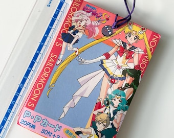 May include: A rectangular Sailor Moon P・P card featuring multiple anime characters in colorful outfits. The card has a purple string attached and text in Japanese. A clear ruler with centimeter markings is in the background.