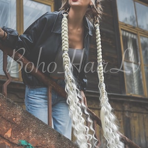 Puede incluir: Dos extensiones de cabello largo rubio platino con secciones trenzadas gruesas en la parte superior que se transforman en mechones ondulados sueltos. Las extensiones están unidas a anillos de metal dorado e incluyen pequeñas cuentas decorativas plateadas.