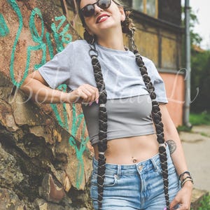 Op de afbeelding: Twee lange, dikke zwarte gevlochten haarextensions met zilverkleurige metalen draadomwikkeling. Deze extensions zijn ontworpen om aan het haar te worden bevestigd, wat zorgt voor een dramatische, langgerekte look met een opvallend kruispatroon.