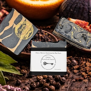 May include: Artisan bar soaps with black and gold marbling, and a gold emblem. The soaps are labeled "Liminal Black Fig & Tobacco". The image includes an orange slice, figs, and spices, suggesting a natural, botanical theme.