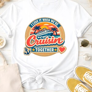 Könnte beinhalten: Weißes T-Shirt mit einem farbenfrohen Grafikdesign. Es zeigt ein Kreuzfahrtschiff, Palmen und den Schriftzug "I love it when we're Cruisin' Together". Ein Anker und ein Herz ergänzen das Design.