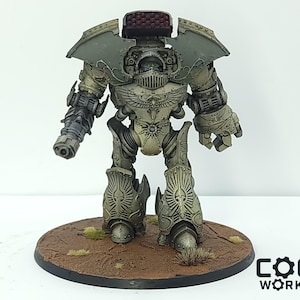 May include: A detailed miniature model of a war machine, painted in shades of gray and tan. The model features intricate armor plating, a large weapon on one arm, and a missile launcher on its back. It stands on a circular base with a brown surface.