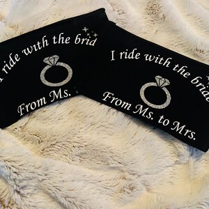 May include: Two black zippered pouches with white text and a diamond ring graphic. One reads "I ride with the brid From Ms." and the other reads "I ride with the bride From Ms. to Mrs."