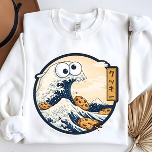 Pode incluir: Camisola branca com um gr&aacute;fico circular de uma onda com olhos arregalados e biscoitos com pepitas de chocolate. O design inclui uma montanha e a palavra japonesa "Cookie".