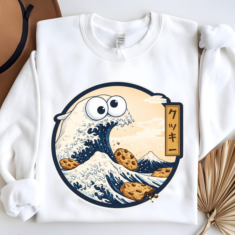 Pode incluir: Camisola branca com um gr&aacute;fico circular de uma onda com olhos arregalados e biscoitos com pepitas de chocolate. O design inclui uma montanha e a palavra japonesa "Cookie".