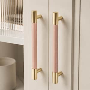 Könnte beinhalten: Zwei Schrankgriffe mit einem zylindrischen rosa Mittelteil und goldfarbenen Enden. Die Griffe sind an einer hellfarbigen Schranktür angebracht. Das Design ist modern und minimalistisch, passend für Küchen- oder Badezimmerschränke.