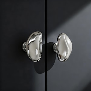 Könnte beinhalten: Ein Set aus drei Keramikbechern mit gesprenkelter, matter Oberfläche. Die Becher sind in Creme-, Hellgrau- und Dunkelgrautönen gehalten. Jeder Becher hat ein schlichtes, minimalistisches Design und einen abgerundeten Griff.