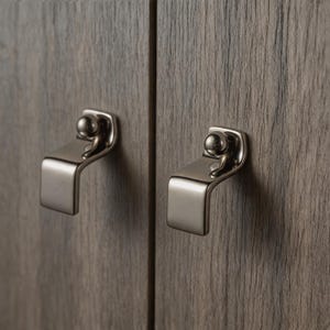 May include: Two brushed nickel cabinet pulls are mounted on a wooden cabinet. Each pull has a curved handle and a small, spherical detail at the top. The cabinet doors have a wood grain texture.