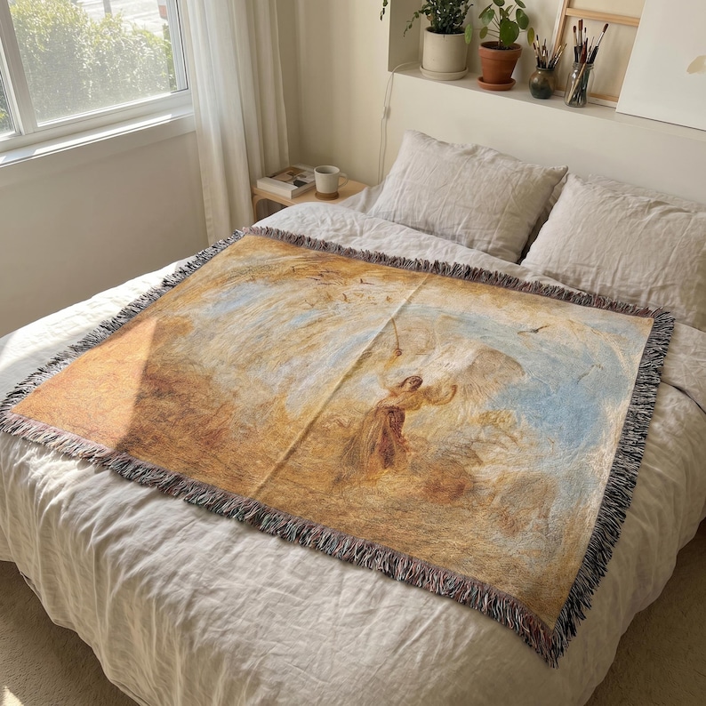 May include: A rectangular woven throw blanket with a detailed painting of a figure in a field with birds and a blue sky. The blanket has a fringed edge and is primarily tan, brown, and blue.