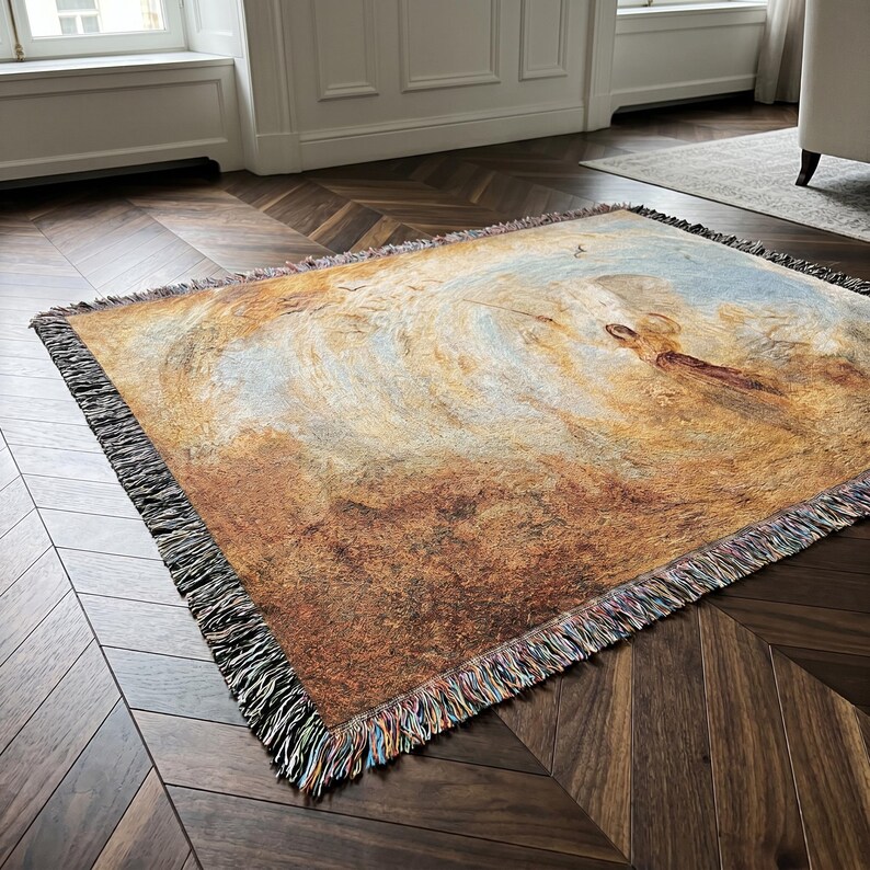 May include: Woven throw blanket featuring a landscape painting in shades of brown, beige, and blue. The artwork depicts a swirling, cloud-like composition. The blanket has a fringed edge with multiple colors.