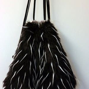 May include: A black and white faux fur tote bag with long, thin strands of fur. The bag has black straps and is hanging from a hook.