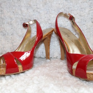 May include: Pair of red patent leather Guess slingback heels with cork platforms and stiletto heels. The shoes have a gold buckle and a peep-toe design. The heels are approximately 4 inches tall.