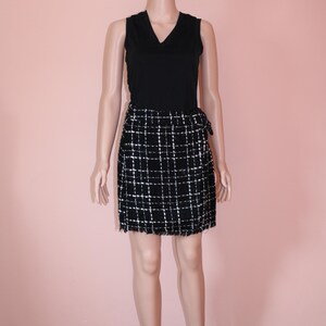 May include: A black sleeveless top paired with a black and white plaid skirt. The skirt has a wrap design with a fringed hem. The outfit is displayed on a mannequin against a pink background.