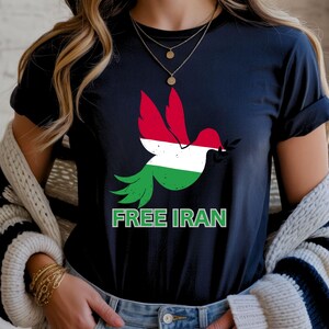 May include: A navy blue t-shirt featuring a dove graphic with the colors of the Iranian flag. The dove holds an olive branch in its beak. The words "FREE IRAN" are printed in green below the dove.