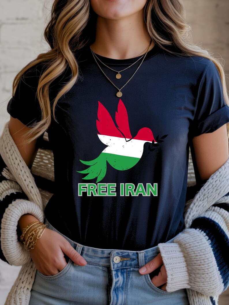 May include: A navy blue t-shirt featuring a dove graphic with the colors of the Iranian flag. The dove holds an olive branch in its beak. The words "FREE IRAN" are printed in green below the dove.