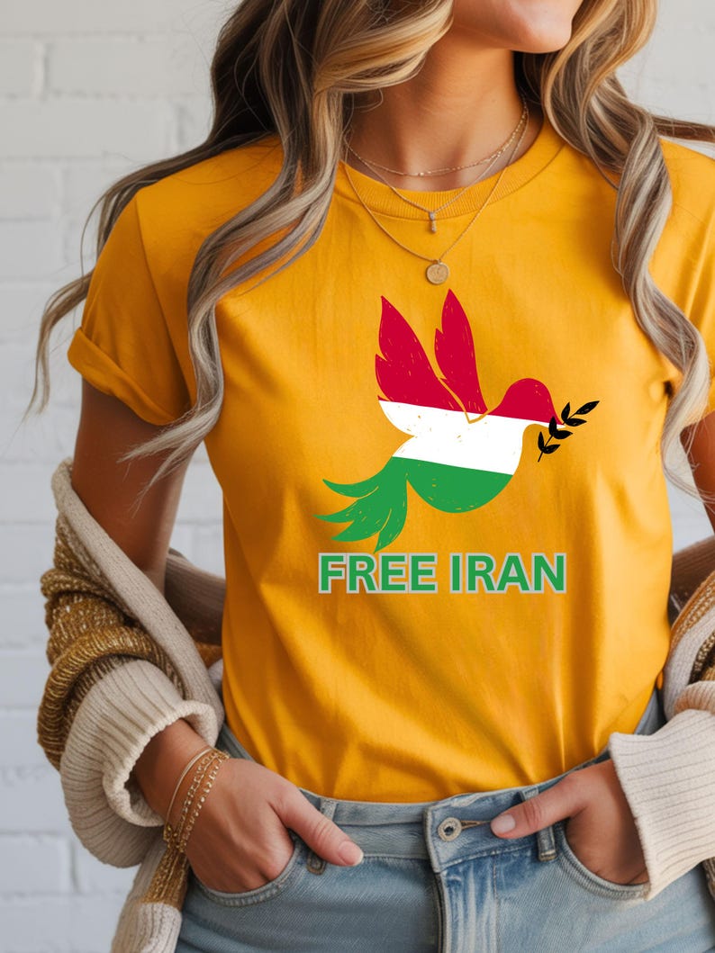 May include: Mustard yellow t-shirt featuring a dove design with the colors of the Iranian flag. The dove holds an olive branch and the words "FREE IRAN" are printed below the bird in green.