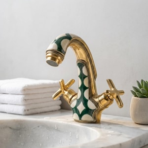 May include: A brass bathroom tap featuring a curved spout and two cross-shaped handles. The tap body is decorated with a repeating pattern of white and dark green geometric shapes. The metal finish is polished gold-toned brass.