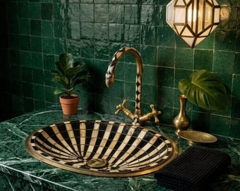 May include: An oval sink basin featuring a black and white radial striped pattern, paired with a matching curved faucet. The setup includes a small potted plant, a brass vase, a black textured towel, and a geometric pendant light fixture.