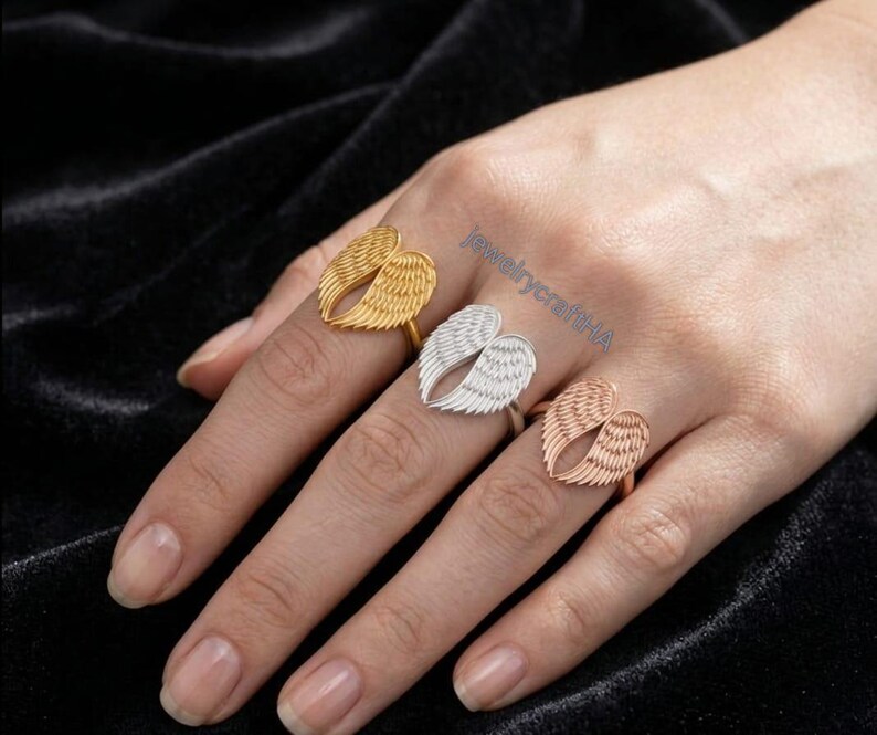 May include: Three rings featuring angel wing designs in gold, silver, and rose gold tones. Each ring displays detailed feather textures on the wings. The text jewelrycraftHA is visible in blue lettering across the center of the image.