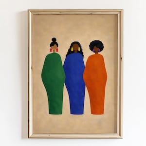 May include: Framed art print featuring three figures in solid-colored dresses: green, blue, and orange. Each figure has a different hairstyle and earrings. The artwork is set against a tan background and framed in a light-colored wood.