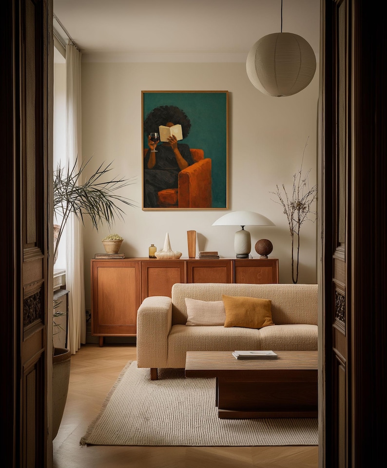 May include: A living room featuring a beige textured sofa with two throw pillows, a wooden coffee table, and a wooden sideboard. Above the sideboard hangs a framed painting of a person reading a book while holding a glass of wine in an orange chair.