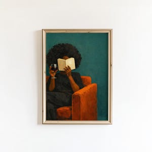 May include: A framed wall art print depicting a person with dark skin and voluminous hair sitting in a bright orange armchair. The person wears a black shirt, holds an open book in front of their face, and holds a glass of red wine in one hand.