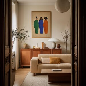 May include: A framed art print featuring three figures in green, blue, and orange robes. The artwork hangs above a wooden cabinet and a beige sofa with throw pillows. A paper lantern and a table lamp are also visible.