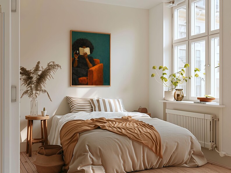 May include: A rectangular wall art print featuring a person with dark curly hair sitting in an orange armchair, holding a book and a glass of red wine against a dark teal background, displayed in a light wood frame above a bed with neutral bedding.
