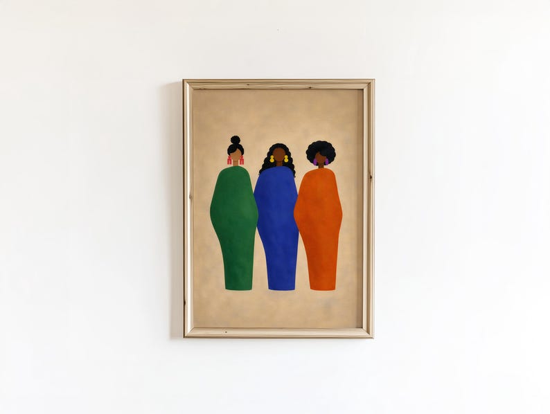 May include: Framed art print featuring three figures in solid-colored dresses: green, blue, and orange. Each figure has a different hairstyle and earrings. The artwork is set against a tan background and framed in a light-colored wood.