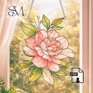 Puede incluir: Vidriera floral que representa una gran flor rosa con hojas verdes y amarillas, suspendida por una cadena. El fondo es una escena exterior borrosa. Las iniciales "SM" son visibles en la esquina superior izquierda.