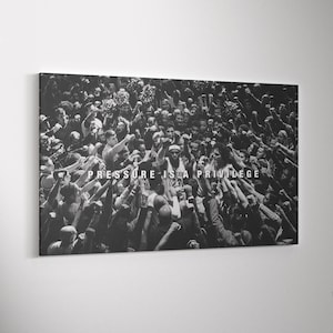 Könnte beinhalten: Ein rechteckiger Schwarz-Weiß-Leinwanddruck, der eine überfüllte Basketballarena zeigt, mit einem zentralen Spieler, der ein Trikot mit der Nummer 23 trägt. Der Text PRESSURE IS A PRIVILEGE ist in weißen Großbuchstaben in der Mitte aufgedruckt.