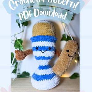 Puede incluir: Muñeca de ganchillo hecha a mano con una cara sonriente, cuerpo a rayas azules y blancas y brazos marrones. Sostiene un objeto rectangular marrón con una cara sonriente. El texto "Crochet Pattern! PDF Download" está encima de la muñeca.