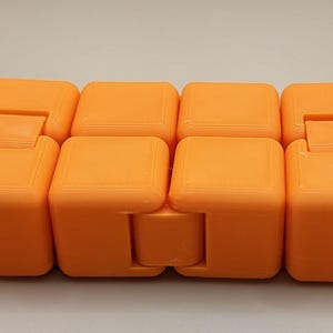 May include: An orange fidget toy with eight connected, cube-shaped blocks. Each block is a solid orange color and has a rounded top. The blocks are connected by hinges, allowing them to move and bend.