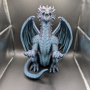 May include: A detailed, blue-green dragon figurine with outstretched wings and a textured, scaly appearance. The dragon is seated, with its claws visible, and has a detailed head with a slightly open mouth. The figurine is likely made of a durable material.