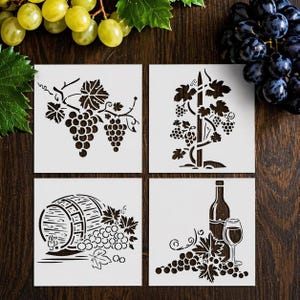May include: Four square stencils with wine-themed designs. The stencils feature images of grape vines, a wine barrel, and a wine bottle with a glass. The stencils are white and set against a dark wood background, with fresh grapes in the corners.