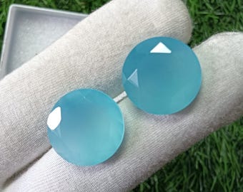 May include: Two round, faceted, light blue gemstones with a smooth, polished surface. The stones exhibit a translucent quality and a circular cut, reflecting light on their top facets. They are presented side by side, showcasing a consistent color.