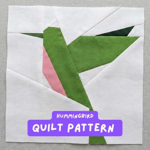 Könnte beinhalten: Ein quadratischer Quiltblock mit einem Kolibri-Design. Der Vogel besteht aus grünen, rosa und weißen Stoffstücken. Der Text "HUMMINGBIRD QUILT PATTERN" wird auf einem lila Banner am unteren Rand des Blocks angezeigt.