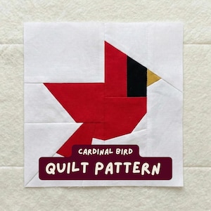 Op de afbeelding: Een vierkant quiltblok met een rood kardinaalvogelontwerp. De vogel staat tegen een witte achtergrond, met een zwart oog en een gouden snavel. De tekst "CARDINAL BIRD QUILT PATTERN" staat op een bordeauxrode banner.