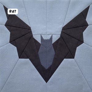 May include: A geometric quilt block featuring a bat design. The bat is depicted with dark gray wings and a lighter gray body, set against a light blue background. The word "BAT" is in a white box in the upper left corner.